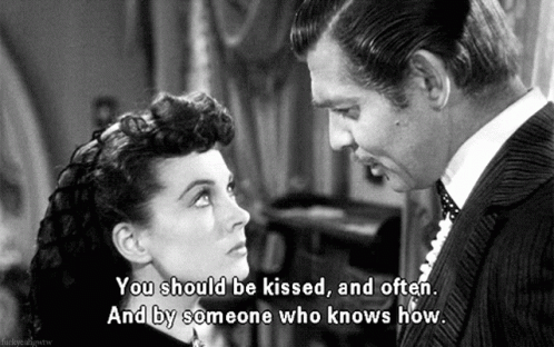The image is from the classic movie Gone with the Wind, featuring Rhett Butler, played by Clark Gable, speaking to Scarlett O'Hara, played by Vivien Leigh. Rhett is leaning toward Scarlett, who looks up at him with a serious expression. The caption reads, "You should be kissed, and often. And by someone who knows how," capturing Rhett's bold and flirtatious demeanor in one of the film's most iconic lines. The scene is in black and white, reflecting the era of the film.